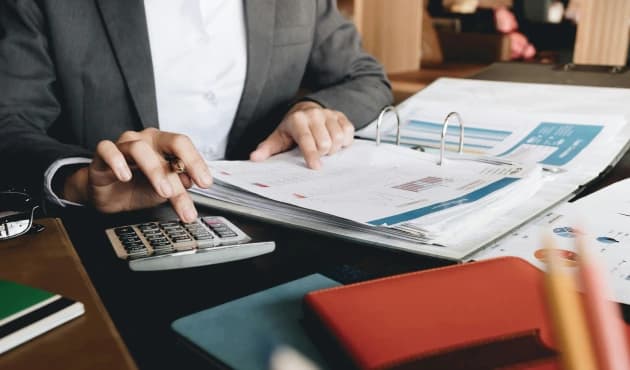 A person reviewing reports while using a calculator to analyse data.