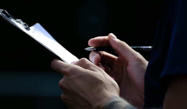Person holding a pen writing on a clipboard