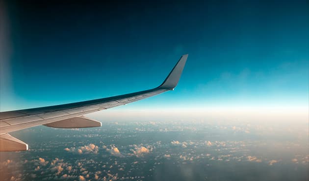View from an airplane window showing an aircraft wing extending over clouds.