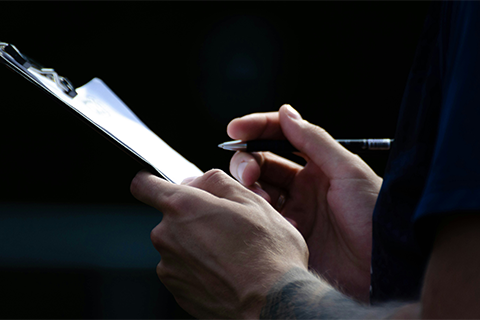 Person holding a pen writing on a clipboard