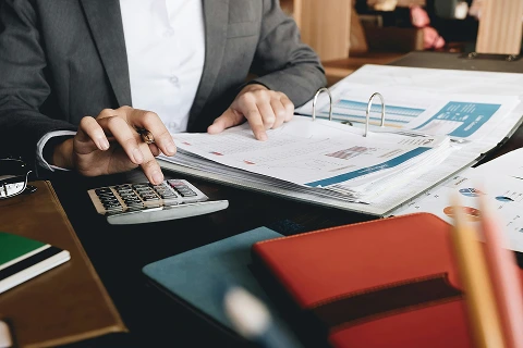 A person reviewing reports while using a calculator to analyse data.