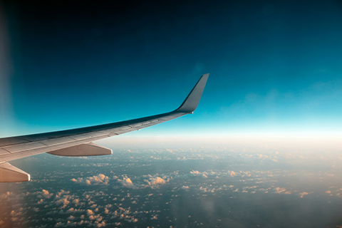 View from an airplane window showing an aircraft wing extending over clouds.